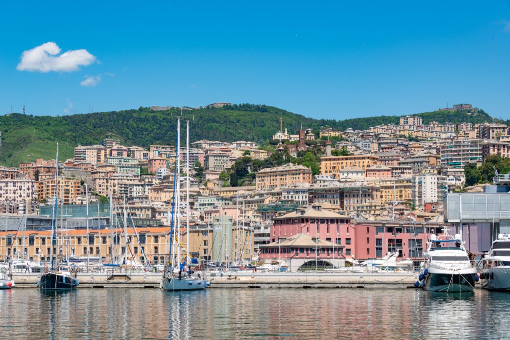 Picturesque view of Genoa's marina with sailboats and a hillside townscape.